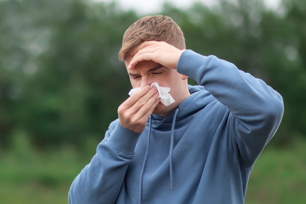 Young man is blowing nose in handkerchief suffering from headache