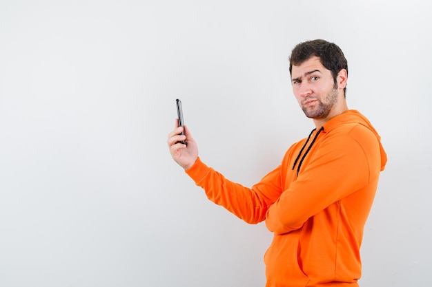 The young man is holding mobile phone is showing funny mimicry on white background