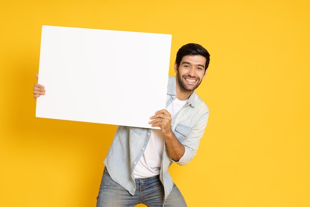 Young man is holding white blank banner on yellow background Looking at camera