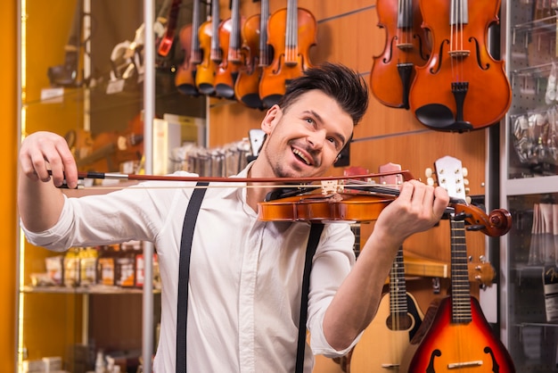 Young man is playing a violin in a music store.