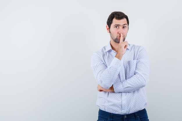 The young man is shoing silent gesture by putting forefinger on lips on white background