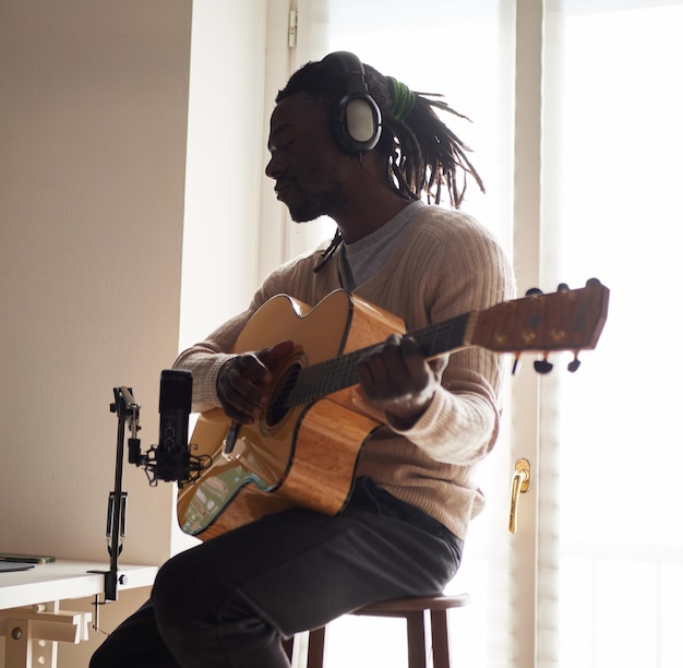 Young man is singing and playing guitar while making an audio recording at home