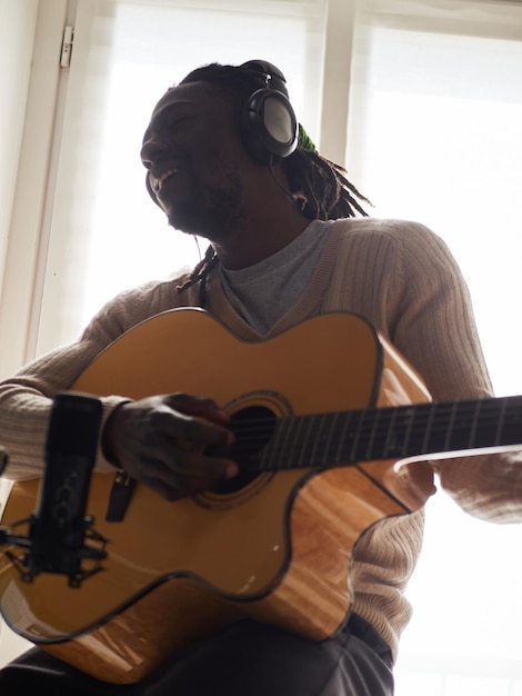 Young man is singing and playing guitar while making an audio recording at home