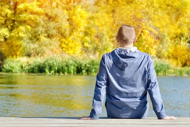 Young man is sitting on the dock Autumn sunny Back view