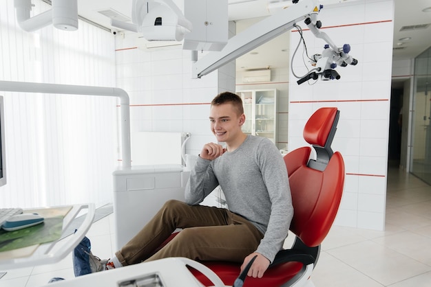 A young man is sitting in a red dental chair and smiling in modern white dentistry Treatment and prevention of caries from youth Modern dentistry and prosthetics