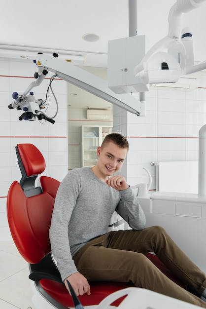 A young man is sitting in a red dental chair and smiling in modern white dentistry Treatment and prevention of caries from youth Modern dentistry and prosthetics