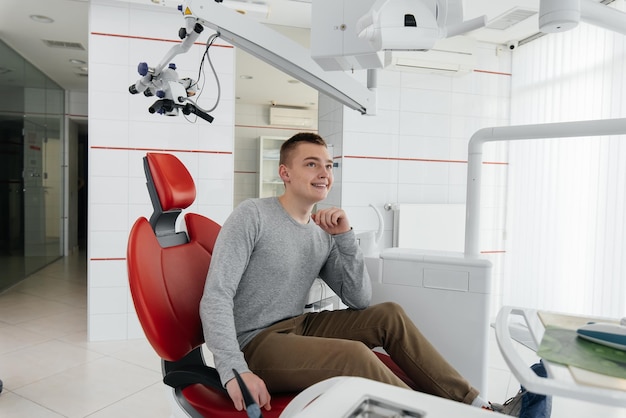 A young man is sitting in a red dental chair and smiling in modern white dentistry Treatment and prevention of caries from youth Modern dentistry and prosthetics