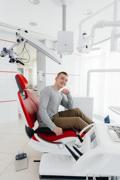 A young man is sitting in a red dental chair and smiling in modern white dentistry Treatment and prevention of caries from youth Modern dentistry and prosthetics