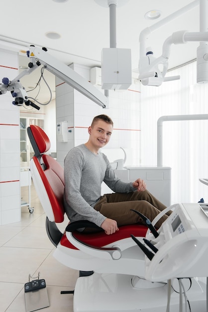 A young man is sitting in a red dental chair and smiling in modern white dentistry Treatment and prevention of caries from youth Modern dentistry and prosthetics