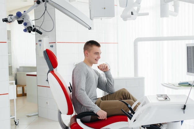 A young man is sitting in a red dental chair and smiling in modern white dentistry Treatment and prevention of caries from youth Modern dentistry and prosthetics