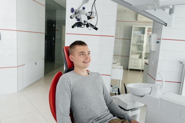 A young man is sitting in a red dental chair and smiling in modern white dentistry Treatment and prevention of caries from youth Modern dentistry and prosthetics