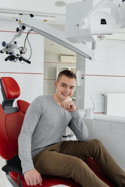 A young man is sitting in a red dental chair and smiling in modern white dentistry Treatment and prevention of caries from youth Modern dentistry and prosthetics