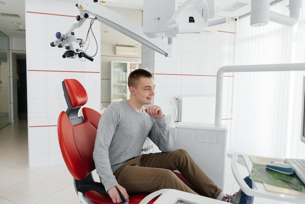 A young man is sitting in a red dental chair and smiling in modern white dentistry Treatment and prevention of caries from youth Modern dentistry and prosthetics