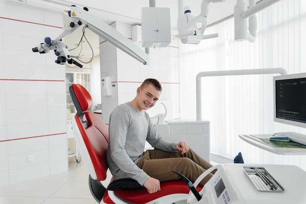 A young man is sitting in a red dental chair and smiling in modern white dentistry Treatment and prevention of caries from youth Modern dentistry and prosthetics