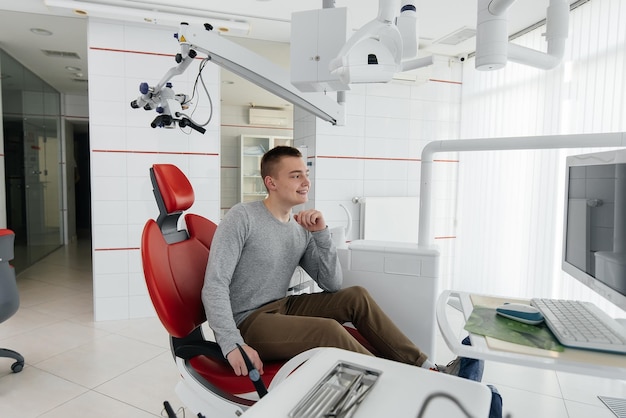 A young man is sitting in a red dental chair and smiling in modern white dentistry Treatment and prevention of caries from youth Modern dentistry and prosthetics