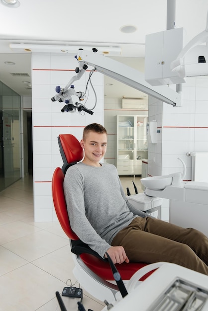 A young man is sitting in a red dental chair and smiling in modern white dentistry Treatment and prevention of caries from youth Modern dentistry and prosthetics