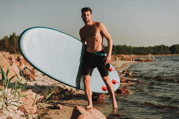 Young Man Is Standing On The Beach With Surf