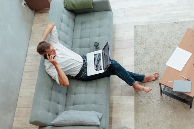 Young man is talking on a smartphone sitting on the sofa