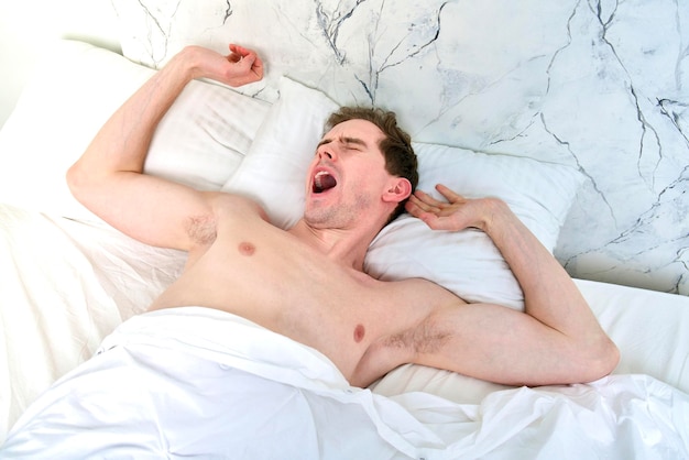 Young man is yawning stretching in bed in bedroom at early morning, yawn, wake up