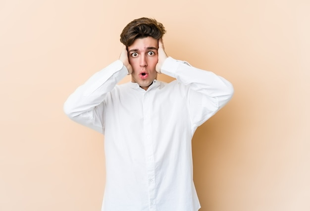 Young man isolated on beige wall being shocked, she has remembered important meeting