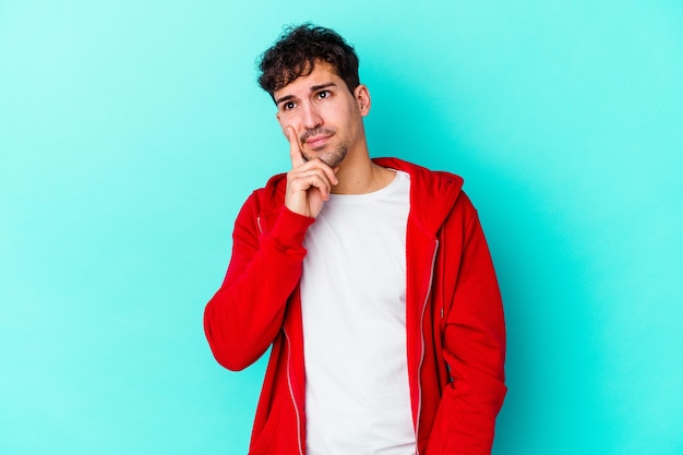 Young man isolated on blue wall contemplating, planning a strategy, thinking about the way of a business