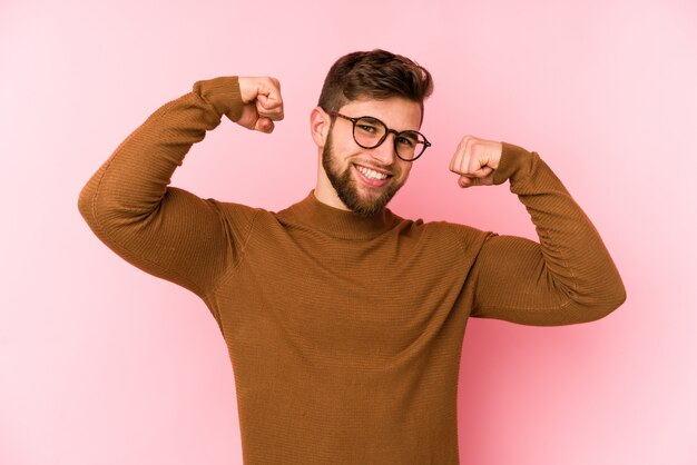 Photo young man isolated on pink wall showing strength gesture with arms, symbol of feminine power