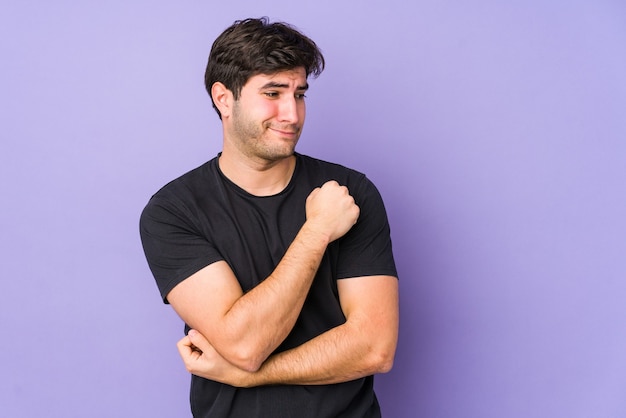 Young man isolated on purple wall confused, feels doubtful and unsure.