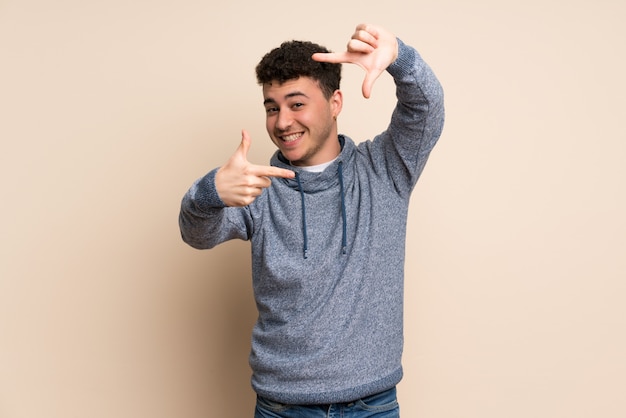 Young man over isolated wall focusing face. Framing symbol