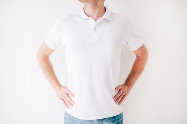 Young man isolated over white wall. Cut view of guy stand alone hands on hips. Wear white shirt.