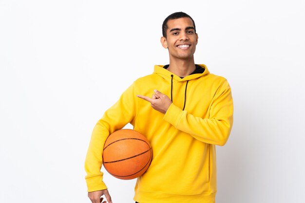 Young man over isolated white wall playing basketball and pointing to the lateral