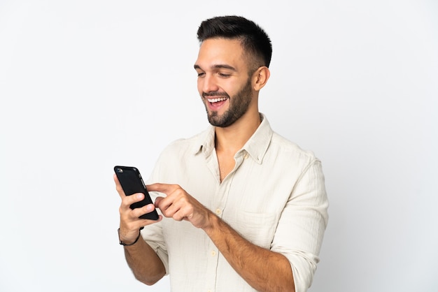 Young man isolated on white wall sending a message or email with the mobile