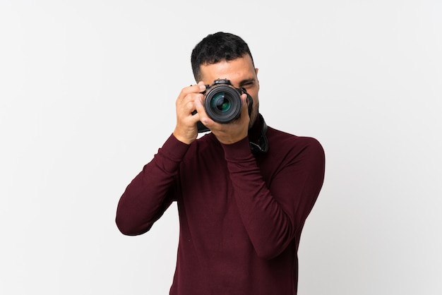 Young man over isolated white wall with a professional camera