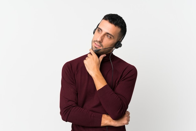 Young man over isolated white wall working with headset looking side