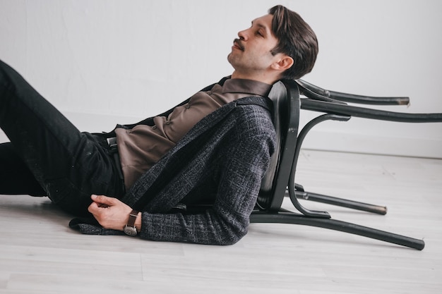 A young man in jeans and a jacket poses against a white wall in the studio