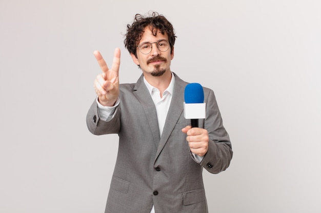 Young man journalist smiling and looking friendly, showing number two