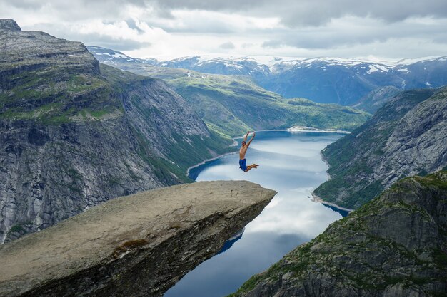 Photo young man jump on the edge trolltunga. norway.