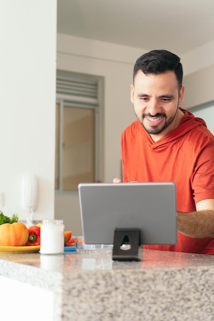 Young man at kitchen preparing a recipe following the steps looking at his tablet