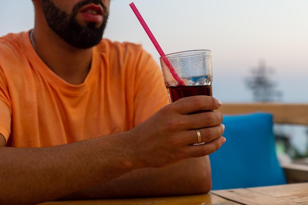 Young man leaning on a bar table while holding a glass with a soft drink and a straw in one hand