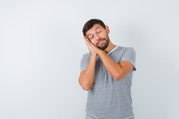 Young man leaning on palms as pillow in t-shirt and looking sleepy. front view.