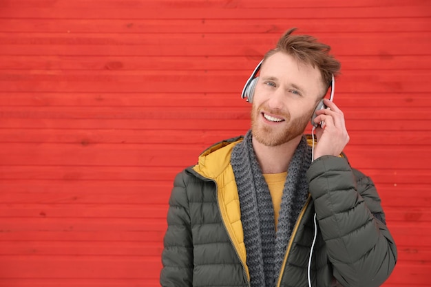 Young man listening to music with headphones against color wall Space for text