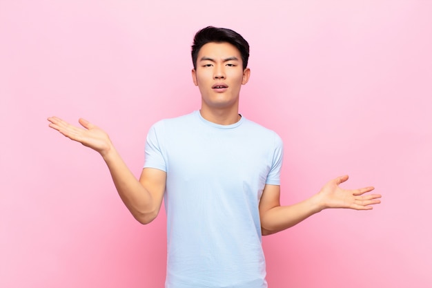 Young man looking puzzled, confused and stressed, wondering between different options, feeling uncertain against color wall