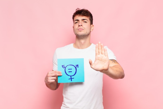 Young man looking serious stern displeased and angry showing open palm making stop gesture