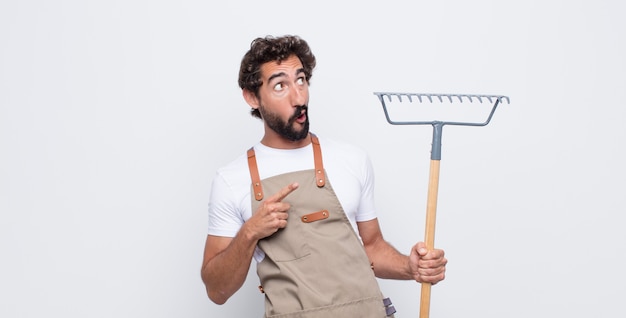 Young man looking shocked, amazed and open mouthed, pointing upwards with both hands to copy space