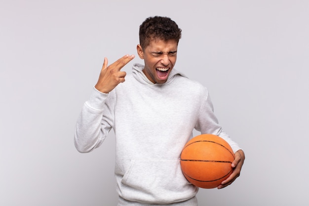 Young man looking unhappy and stressed, suicide gesture making gun sign with hand, pointing to head. basket concept