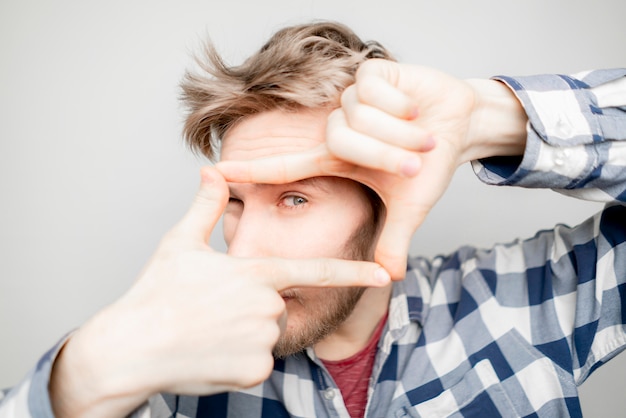 Young man make a hand frame over his face on bright background