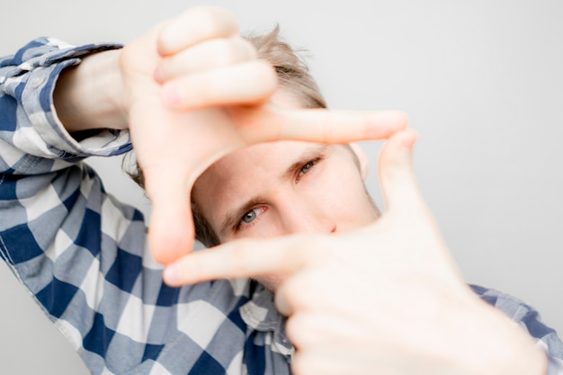 Young man make a hand frame over his face on bright background