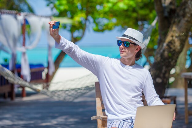 Photo young man make a photo on cell phone at tropical beach 