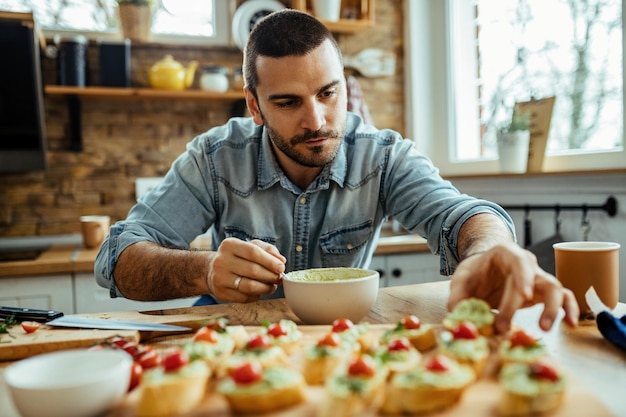 Young man making bruschetta while preparing food in the kitchen