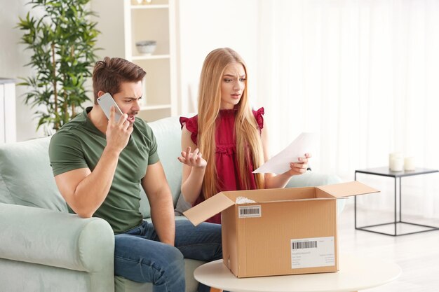 Young man making call about delivered parcel and woman with purchase order sheet at home