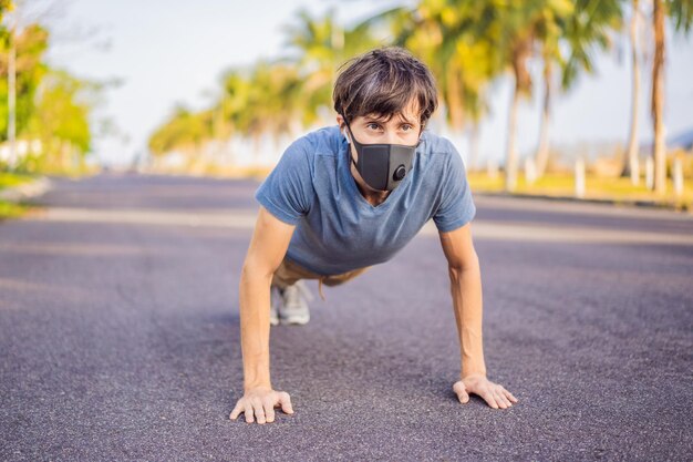 Young man in medical mask performing some workouts in the park during coronavirus quarantine